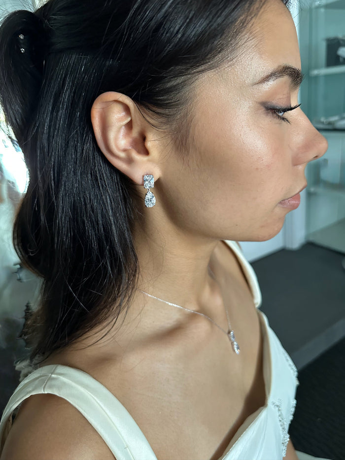 Woman wearing diamond earrings and necklace in a blurred indoor setting