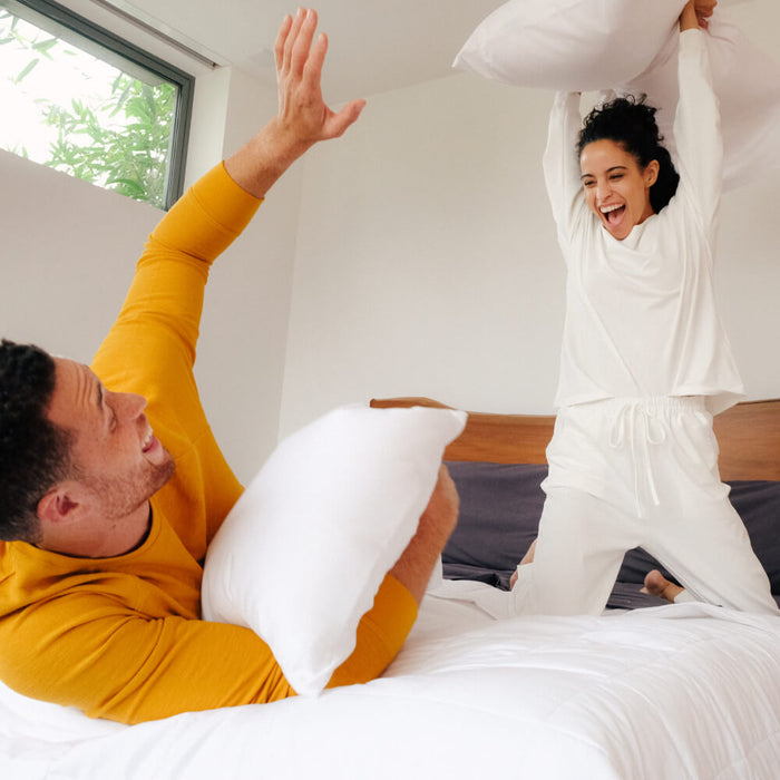 A young couple pillow fighting in a bed made with Slumber Cloud products.