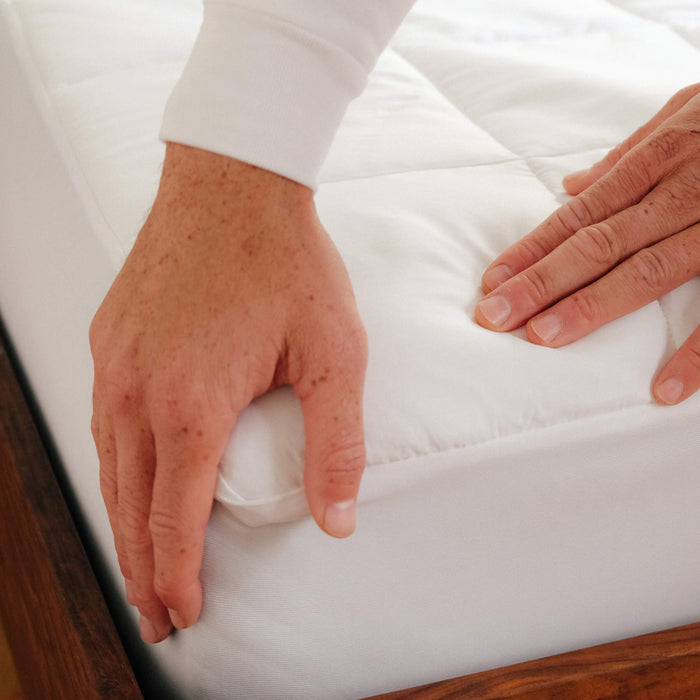 Detailed close up of a man putting the Slumber Cloud Core Mattress Pad on mattress