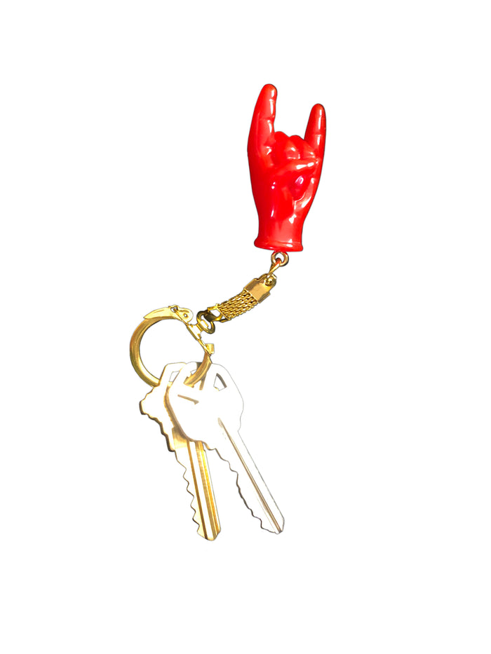 Red hand-shaped keychain making the “rock on” gesture, attached to a gold-colored chain and keyring. The glossy charm blends Italian Malocchio symbolism with rock culture, serving as a bold accessory for protection, style, or gifting.