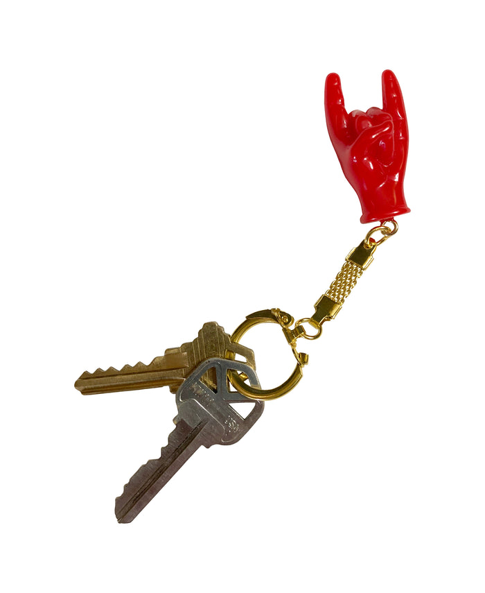 Red hand-shaped keychain making the “rock on” gesture, attached to a gold-colored chain and keyring on white background. The glossy charm blends Italian Malocchio symbolism with rock culture, serving as a bold accessory for protection, style, or gifting.