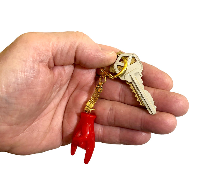 Red hand-shaped keychain making the “rock on” gesture, attached to a gold-colored chain and keyring. The glossy charm blends Italian Malocchio symbolism with rock culture, serving as a bold accessory for protection, style, or gifting.