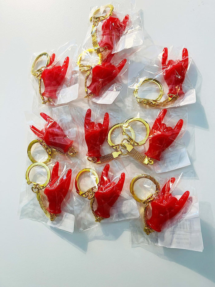 Red hand-shaped keychain making the “rock on” gesture, attached to a gold-colored chain and keyring in pack of 10. The glossy charm blends Italian Malocchio symbolism with rock culture, serving as a bold accessory for protection, style, or gifting.