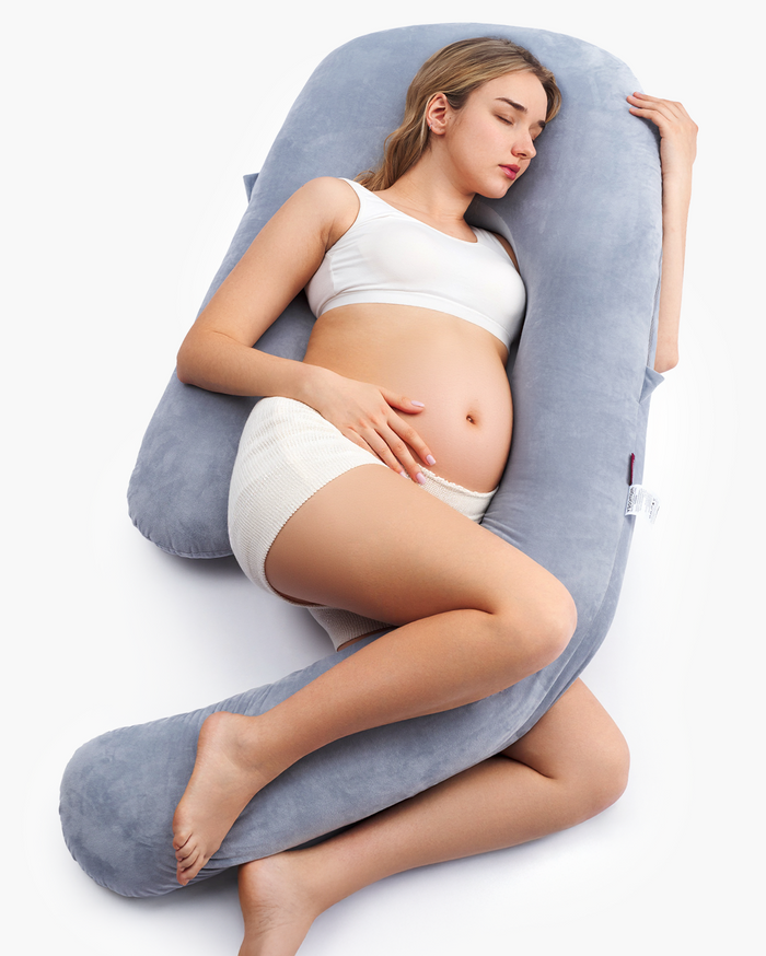 Pregnant woman resting on a grey Momcozy Dreamlign pregnancy pillow, providing support and comfort during sleep.