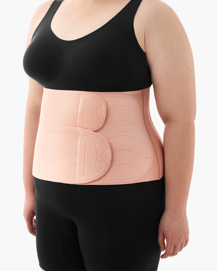 Momcozy Ergowrap Postpartum Belly Band in oyster pink, worn over black activewear, for postpartum support.