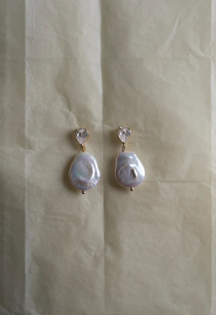 Pair of pearl earrings on a beige fabric background