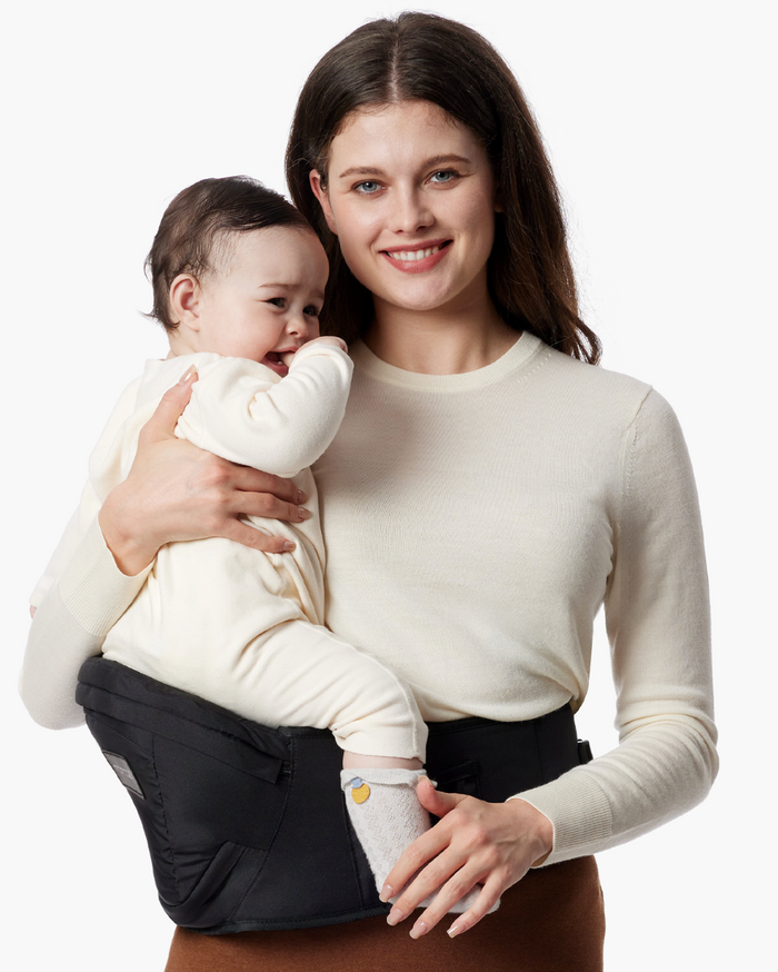 Momcozy Wander360 Hip Seat Carrier: Woman holding baby in a black carrier, babywearing solution for comfort and convenience.