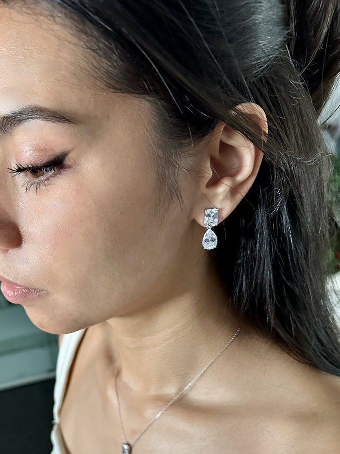 Close-up of a person wearing a silver earring with a clear gemstone.